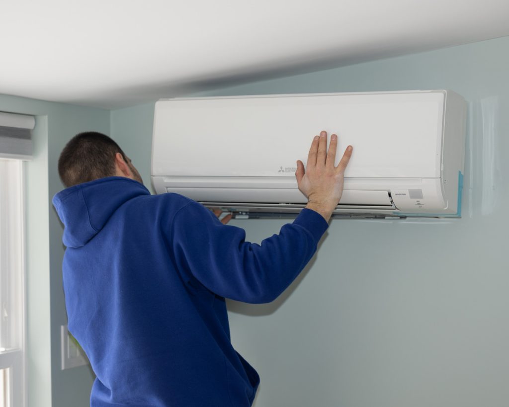 Technician installing a wall-mounted Mitsubishi AC unit.