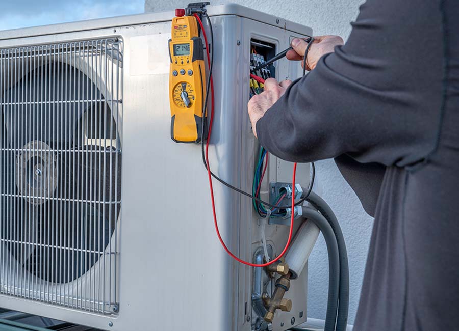Technician testing electrical connections on an outdoor AC unit