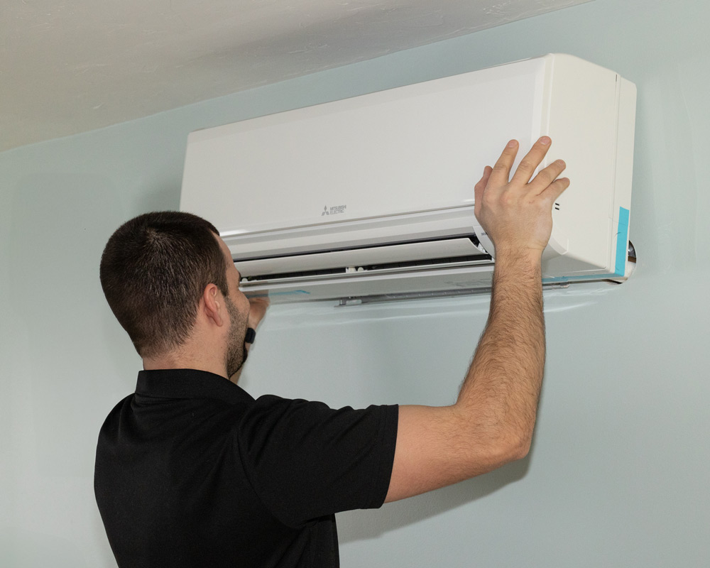 Technician inspecting a wall-mounted Mitsubishi air conditioning unit