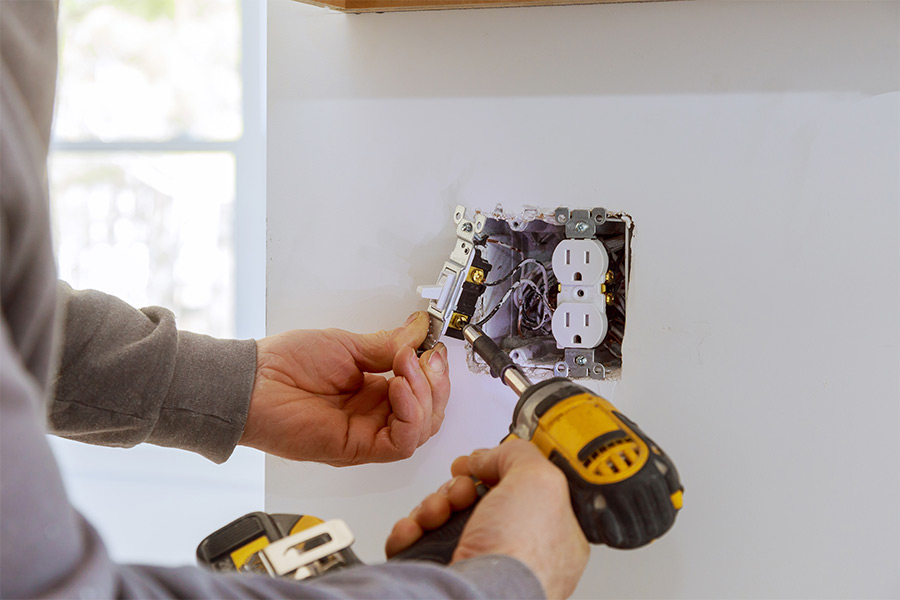 Electrician installing a wall outlet using a drill